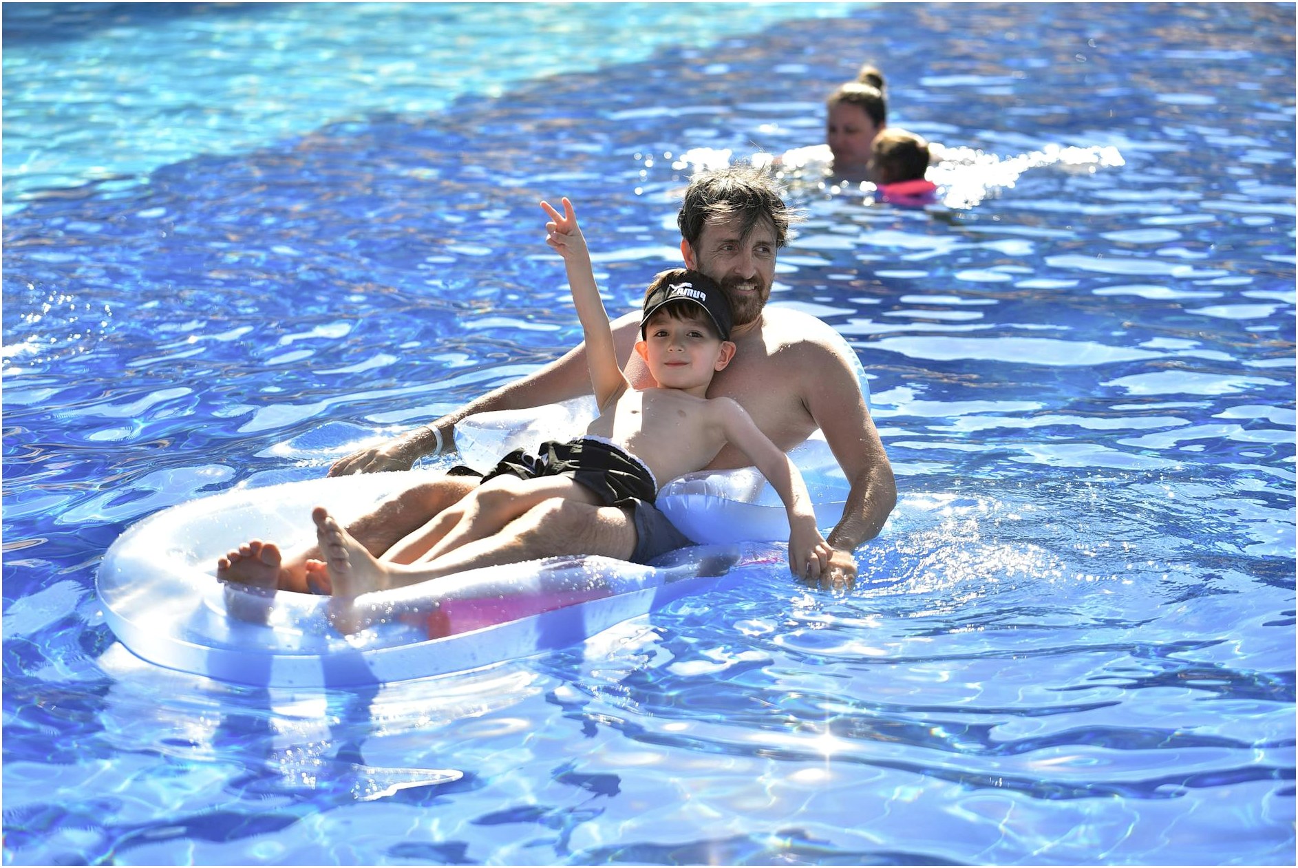 Father and son enjoying summer on an inflatable mattress in a sunny pool.