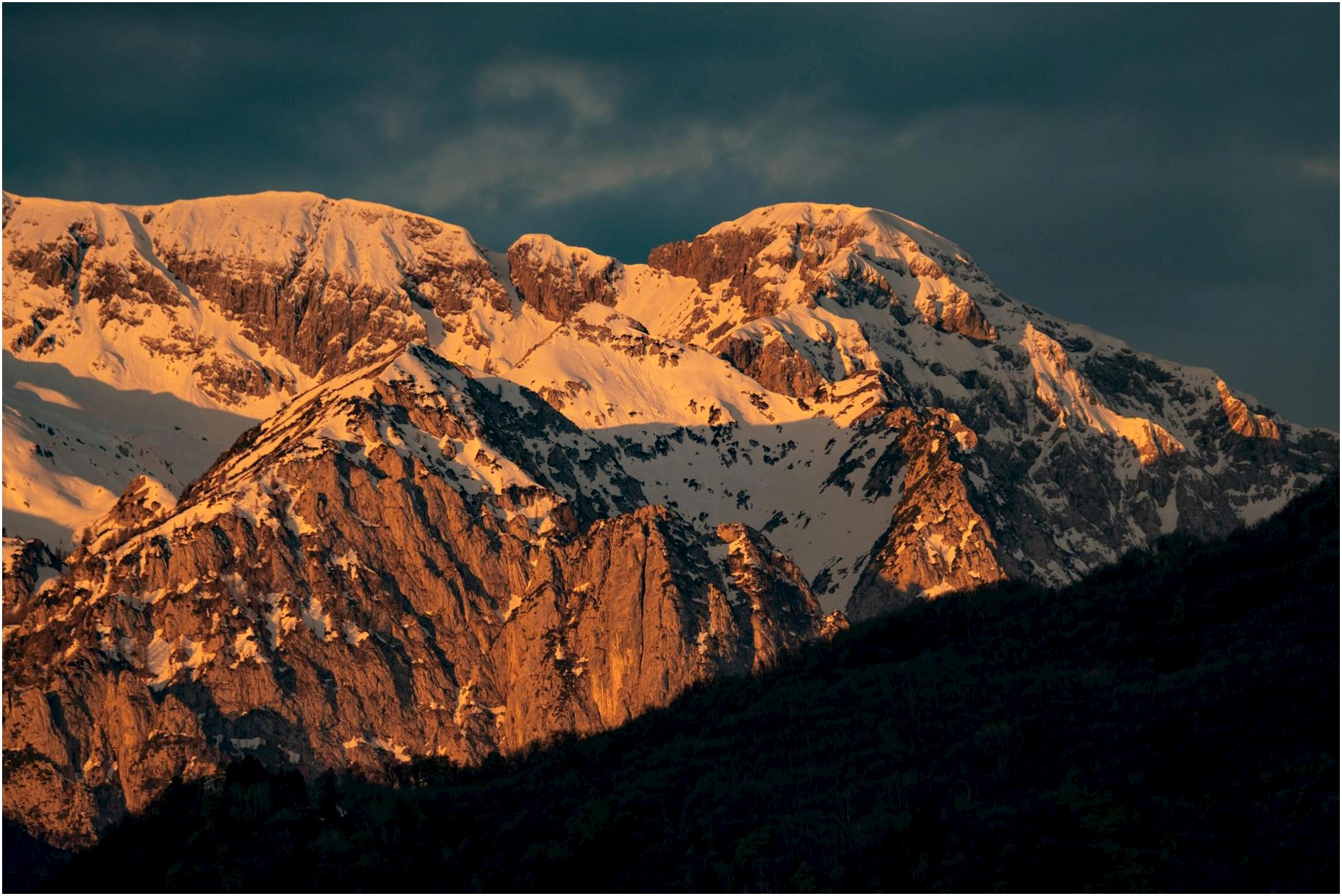 Stunning view of rocky, snow-covered mountains illuminated by sunset light.