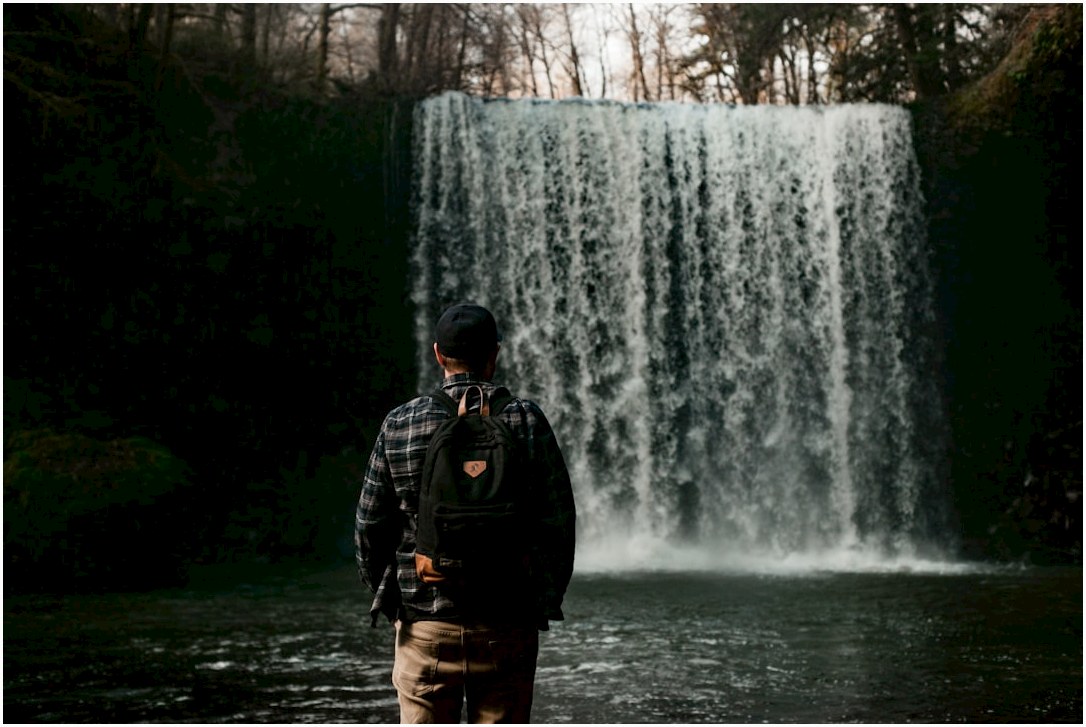 man in black jacket standing in front of waterfalls